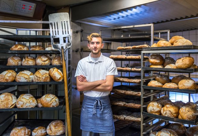 baker posing in his bakery bakehouse in the early morning between fresh baked artisan bread